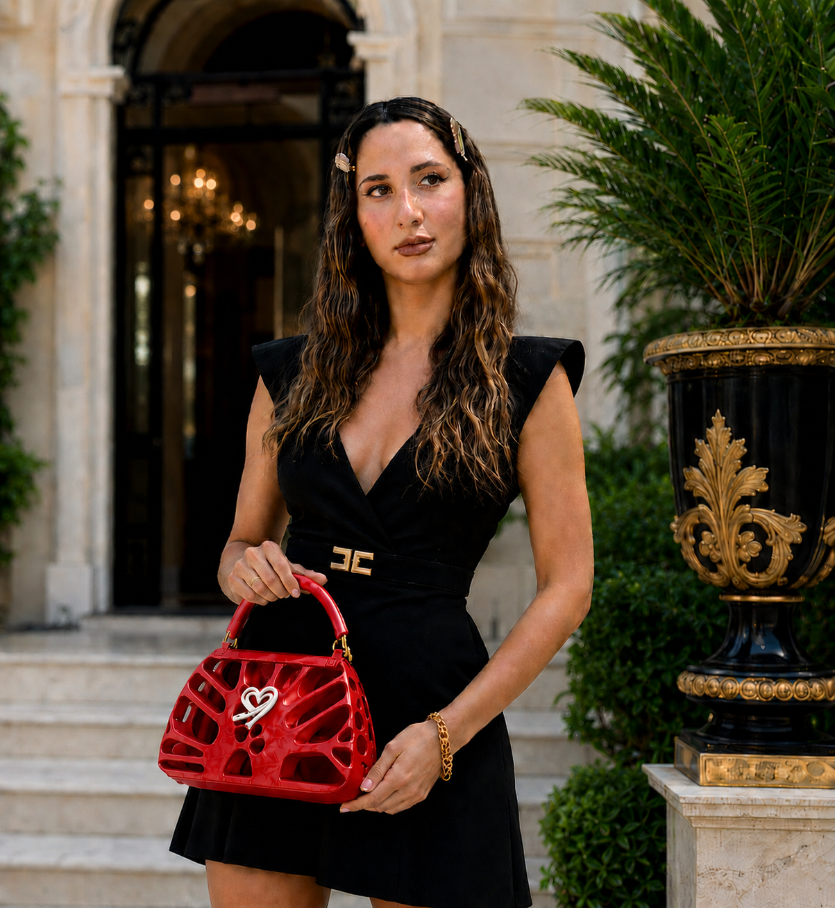 Fjoccola FDR glossy red women’s handbag, a statement 3D printed PLA Silk designer bag featuring a sculptural openwork design, top handle and signature white heart detail, styled with an elegant black dress.