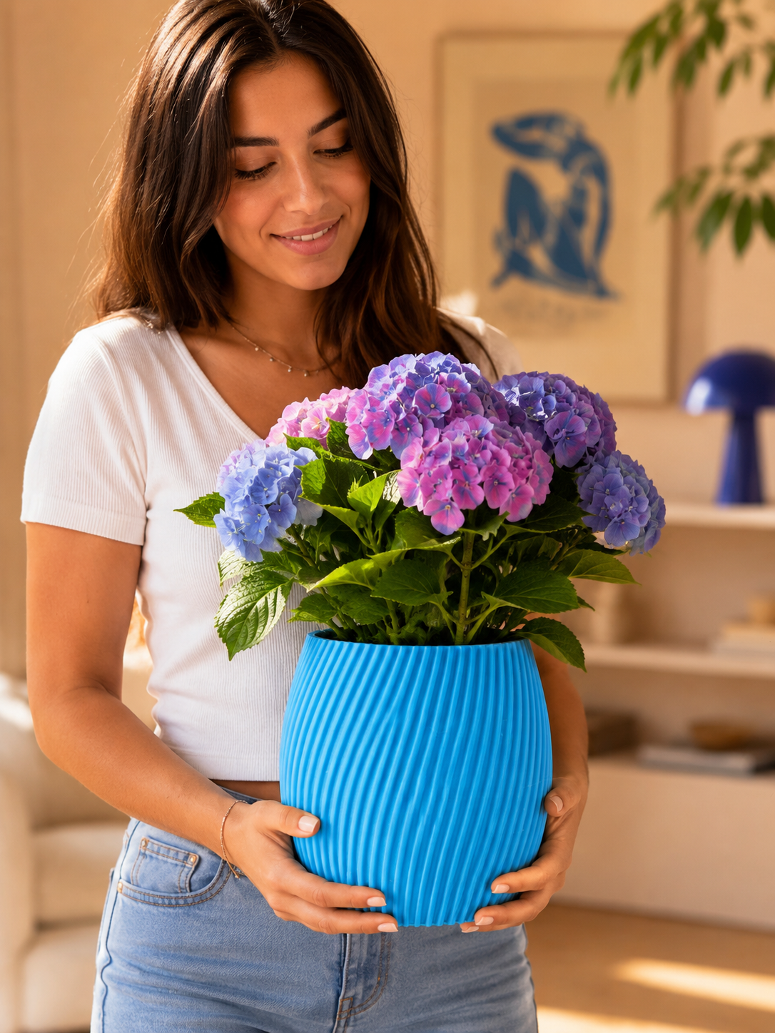 Woman holding large blue decorative planter with colorful flowers, modern indoor plant pot for elegant home decor and contemporary interiors.